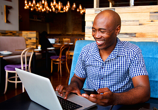 A man sitting at a cafe, with a smile on his face, working on his laptop