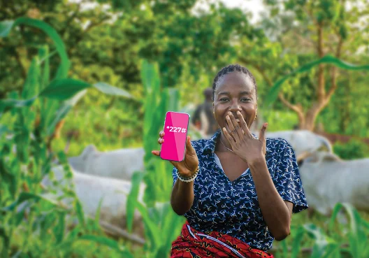 A woman wearing a blue dress and sitting in a garden holds up her cellphone. 