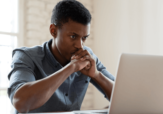 A man clasps his hands in front of his face as a he reads an email sent from a suspicious address.