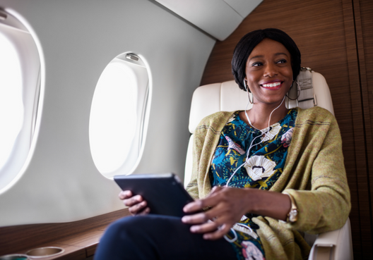 A young professional woman uses a tablet and earphones while flying for business.